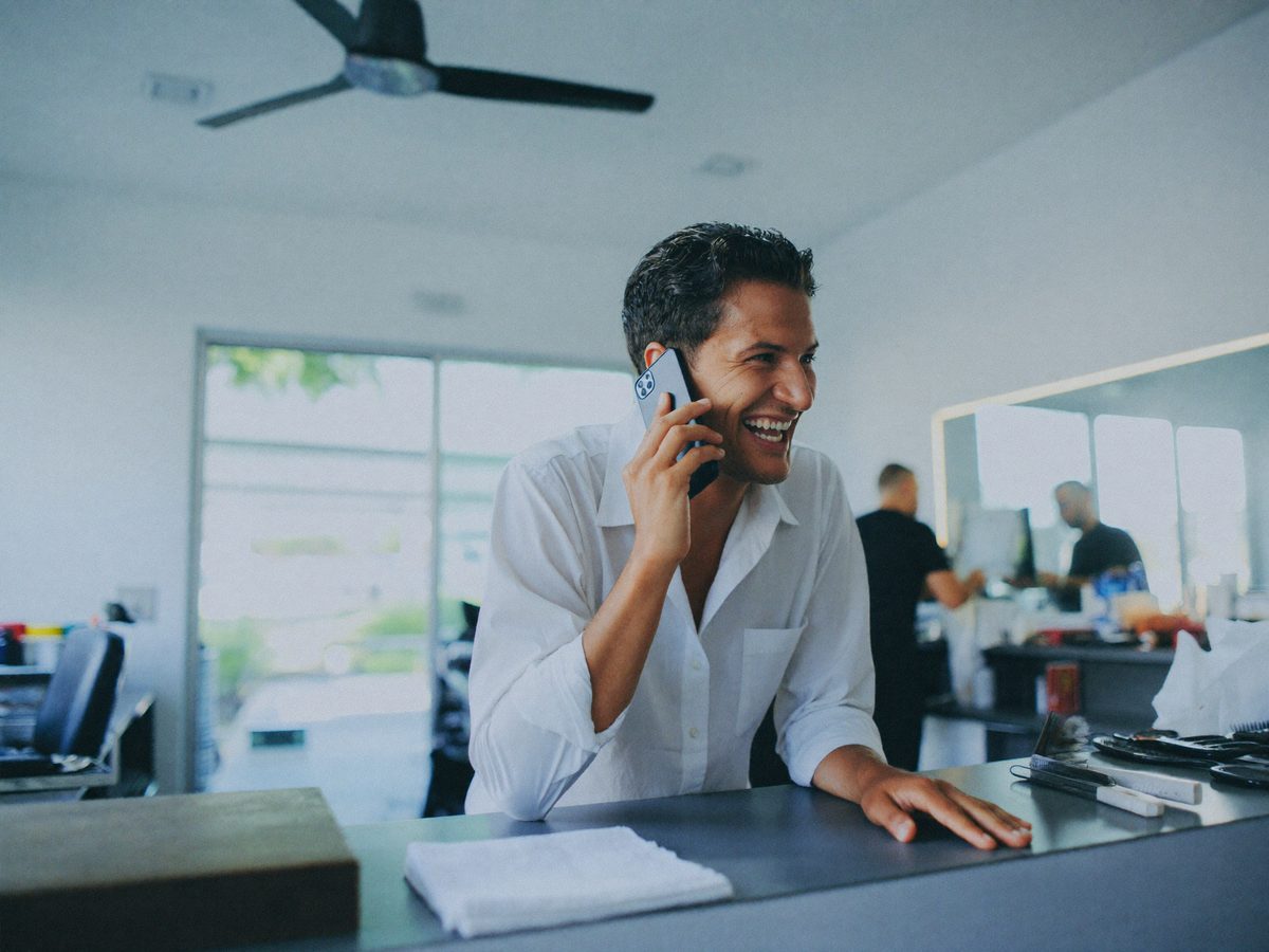 A shop owner on the phone while his assistant handles the schedule